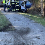 Zerstörter PKW am Straßenrand mit Feuerwehrleuten