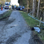 Zerstörter PKW am Straßenrand mit Feuerwehrleuten